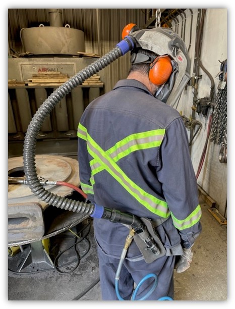 A grinder wears a fresh air supply to improve health and safety in the foundry.